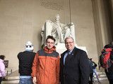 Two people posing in front of a large white statue indoors, one in an orange jacket and one in a dark coat.
