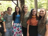 Five people standing together outdoors, smiling at the camera under a shaded structure.