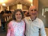 Two smiling people standing indoors at a party, one in a pink floral top and the other in a light shirt