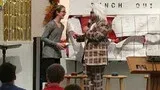 Two people standing by a classroom board, one holding a plaid poster while the other gestures toward it.