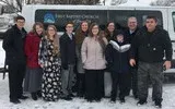 Group posing in winter snow in front of a sign and parked vehicle