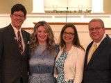 Four people posing together indoors, dressed in formal attire and smiling.