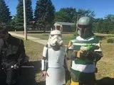 Three people in Star Wars costumes standing outdoors, including a white droid and green-and-gray armor.