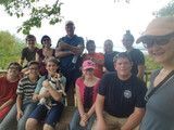 Group of people sitting on steps outdoors, smiling at the camera, with a tree in the background.