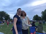 Two people posing together outdoors at a park on a cloudy day, with a crowd in the background
