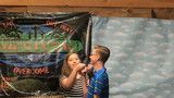 Two children at a science fair stand beside a rocket model and launch display