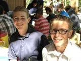 Two smiling people seated at a crowded outdoor table, with drinks and other diners in the background
