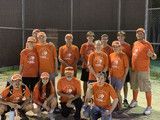 Group of people in orange shirts posing outdoors at night on a sports field