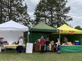 Outdoor fair booths under white, green, and yellow canopies with people serving at tables