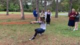Person swinging on a rope in a park while others watch nearby under trees