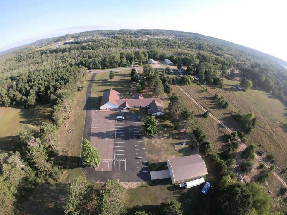 Aerial view of a rural parking lot, buildings, and surrounding trees under a bright sky