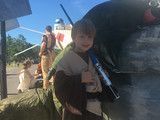 Child holding a drink cup beside a car at an outdoor campsite