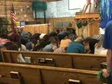 People seated in a church pew during a service, facing the pulpit and American flag.