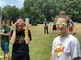 People in a grassy field wearing colorful masks and glasses, smiling at the camera