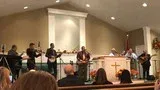 Band performing on a church stage with singers, musicians, and a pulpit under bright lights.