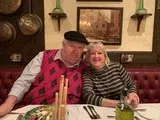 Two people smiling at a restaurant table, with one wearing a pink sweater and black cap.