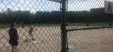 People standing near a chain-link fence by a sports field, with one holding a dog.