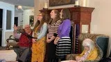 People gathered in a living room, singing together near a fireplace.