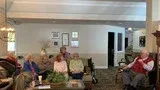 People seated in a bright community room, listening to a woman speaking at the front.