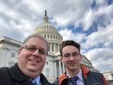 Two people smiling for a selfie in front of the U.S. Capitol building