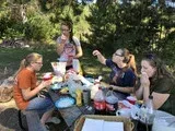 People sharing food and drinks at an outdoor picnic table under trees