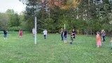 People standing in a grassy park near a row of white poles and trees