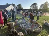 People gathered outdoors around a smoky fire pit beside logs and a suburban house