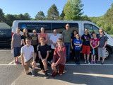 Group of people posing beside a white van in a parking lot on a sunny day