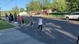 People walking along a sunny suburban street with cars parked nearby.