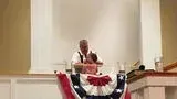 Person speaking at a church pulpit decorated with red, white, and blue bunting