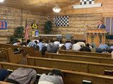 People seated in a wooden church or lodge hall facing the front, with checkered flags and banners on the wall.