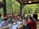People seated at picnic tables under a wooden pavilion, working together outdoors.