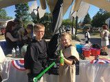 Two people in costumes holding lightsabers at an outdoor event table with patriotic decorations.