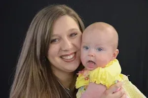 Woman holding a baby in a yellow outfit against a dark background