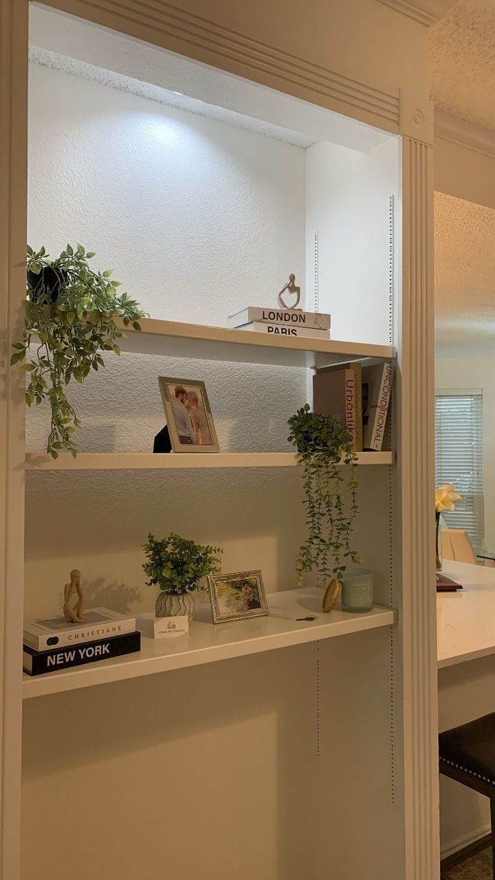 White wall shelves with potted plants, books, and decor in a softly lit hallway alcove
