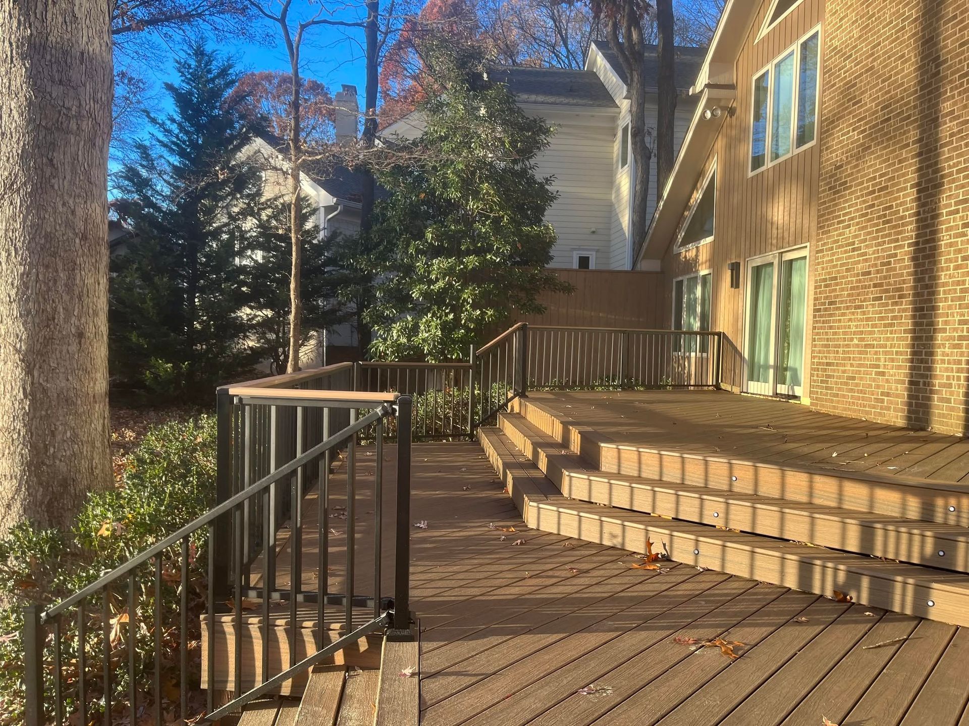 Brick patio deck with black railing beside a house, lined with steps and autumn trees in sunlight