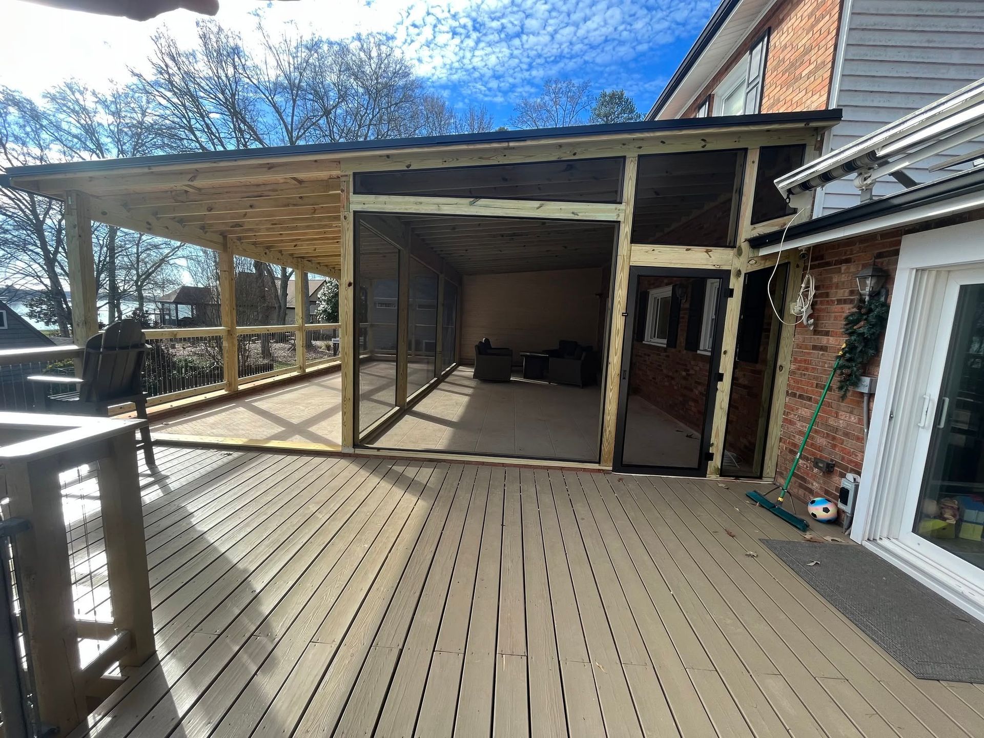 Wooden deck with covered patio and open framing beside a brick house on a sunny day