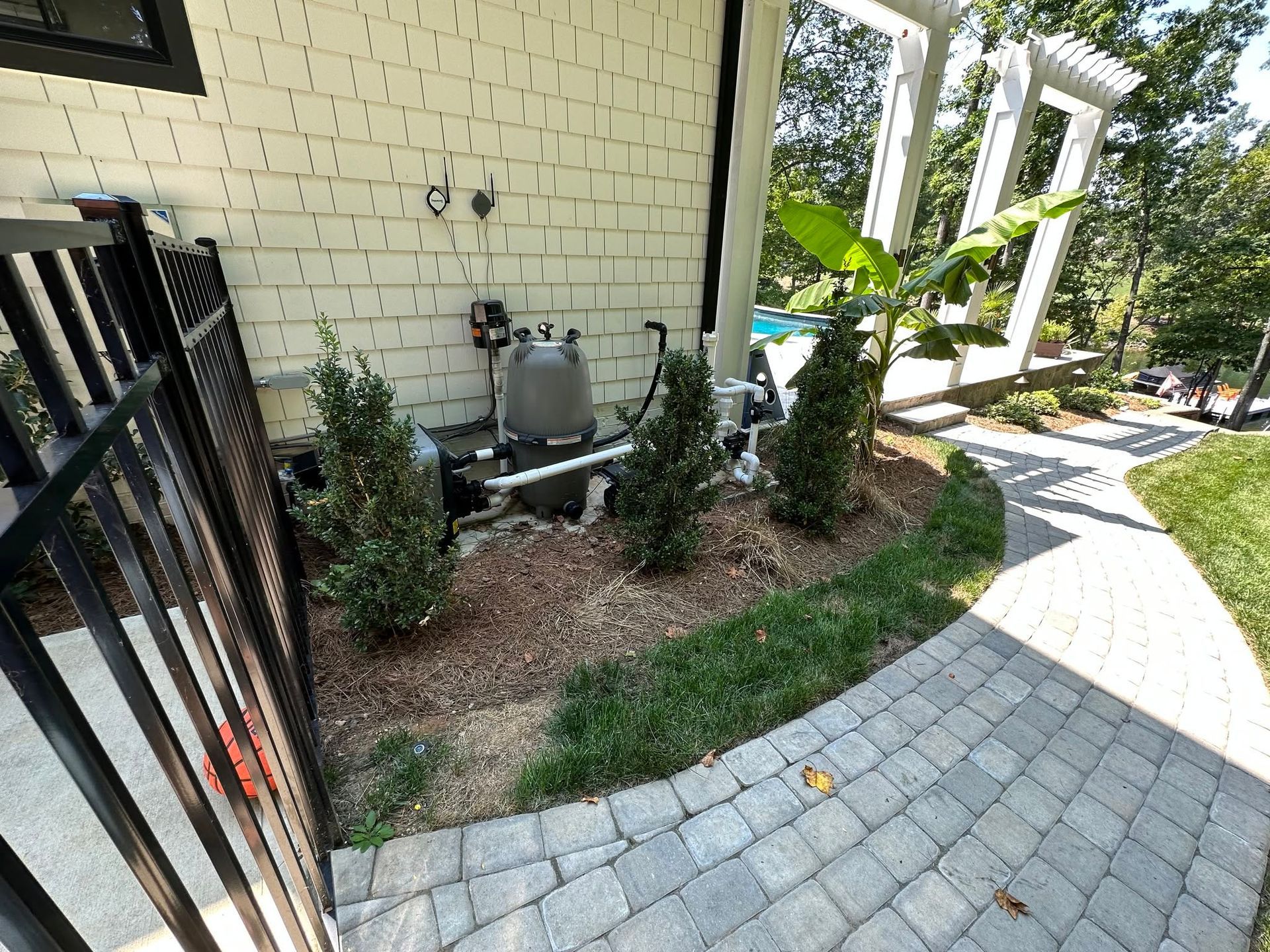 Curved brick walkway beside a white brick house, with shrubs and a garden bed along the side.