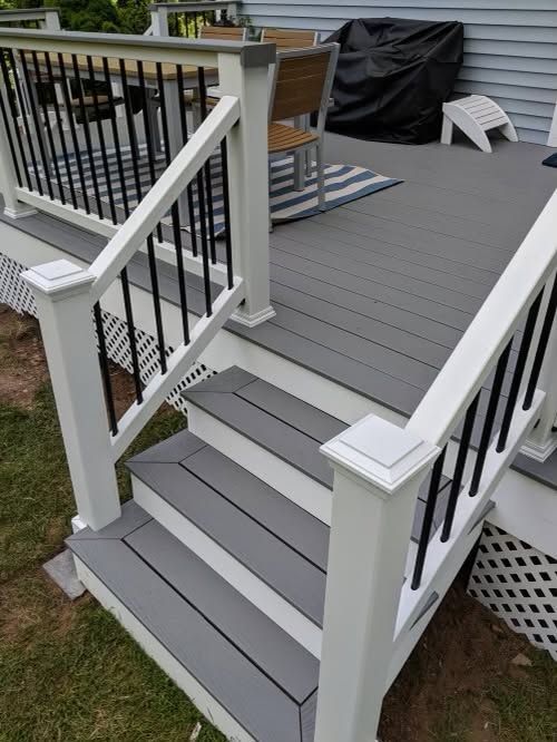 Gray porch steps with black railings leading to a deck, with outdoor furniture and a grill cover in the background