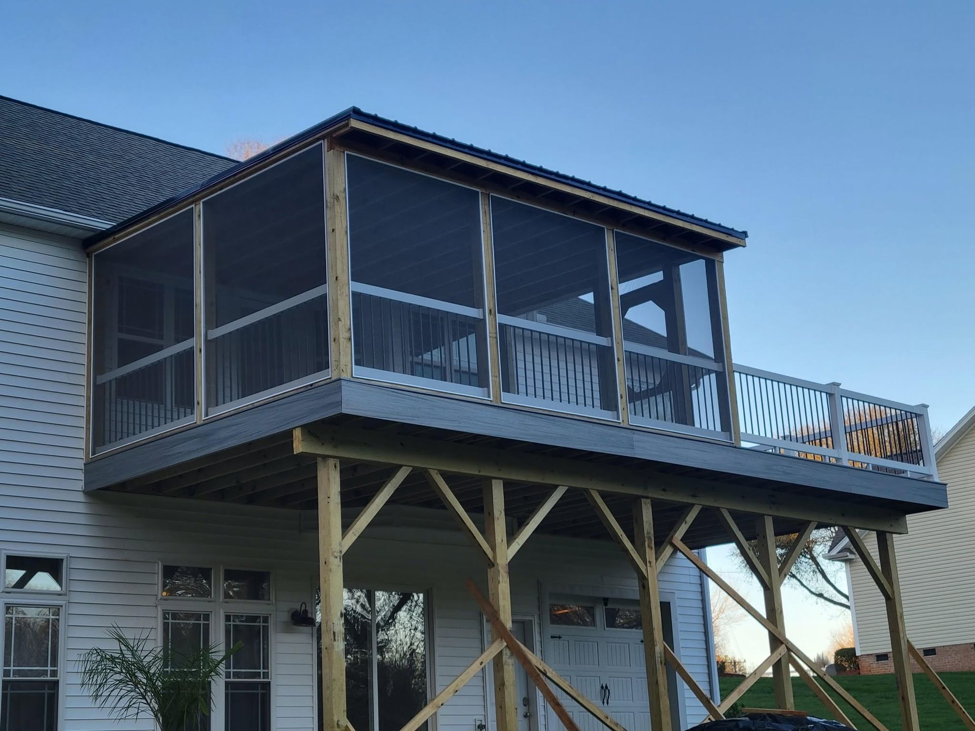 Raised house porch under construction with wooden supports, screened walls, and blue railings