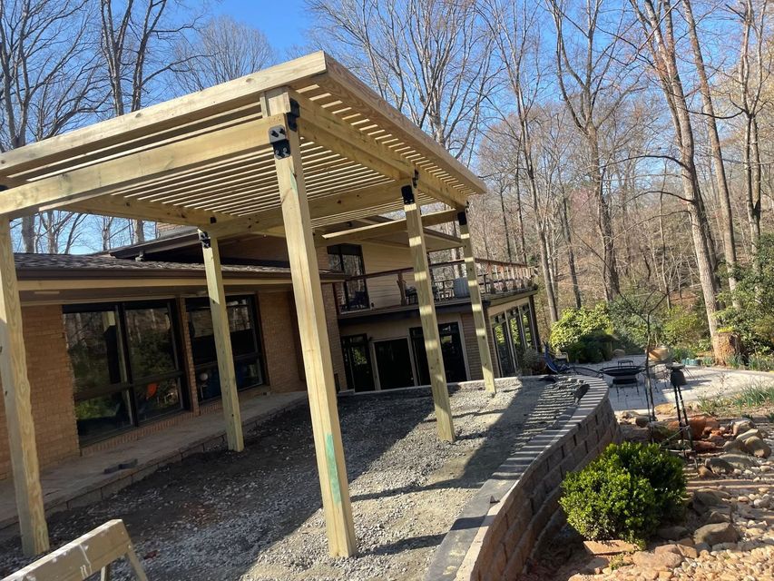 Covered outdoor patio with wooden pergola, stone wall, and leafless trees in the background