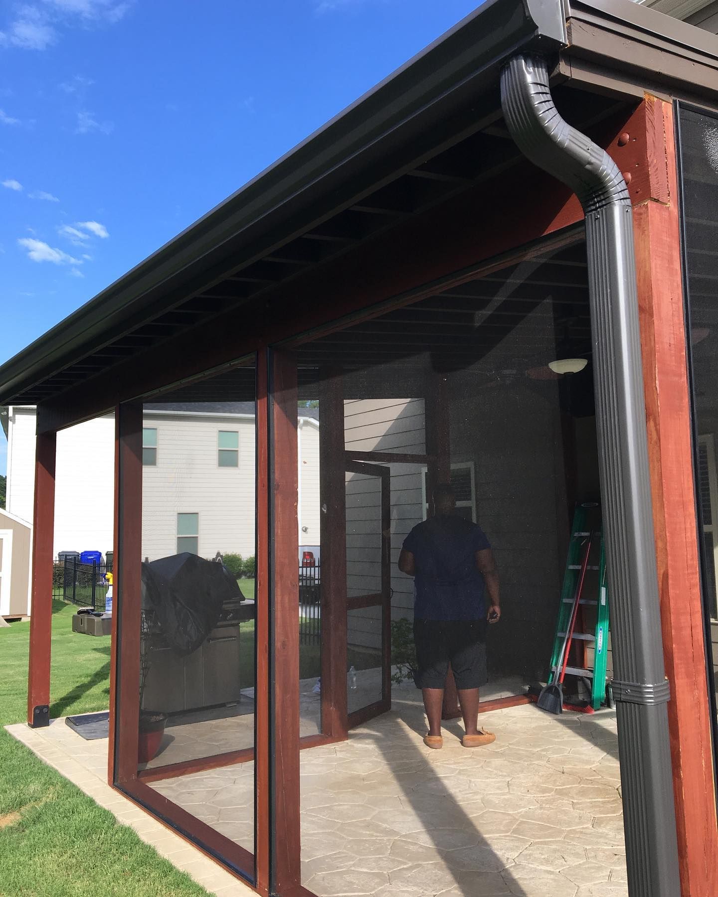 Covered patio with a screened enclosure and two people standing inside near a ladder