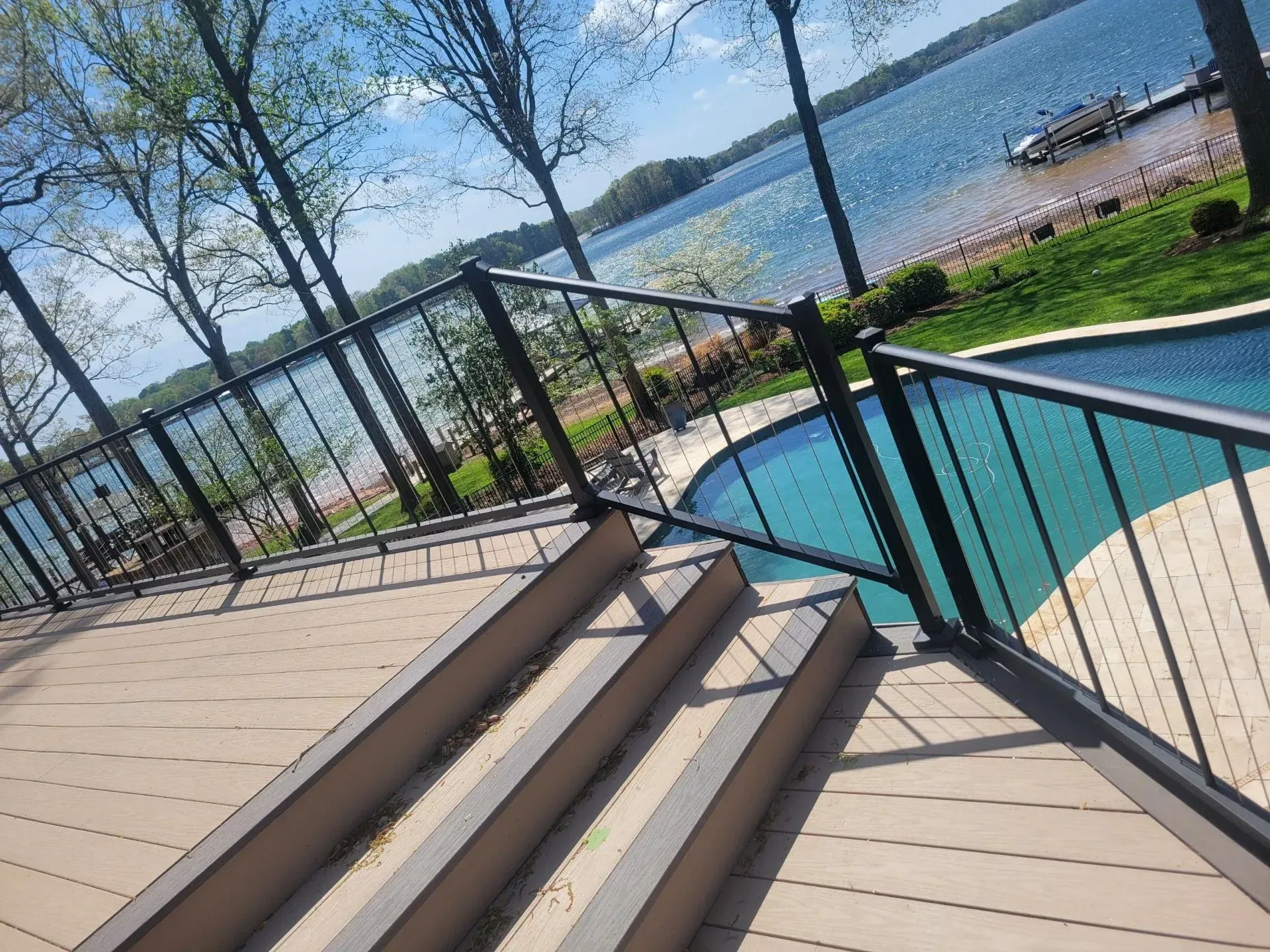 Deck stairs overlooking a blue pool and lake, with black railings and sunny outdoor scenery