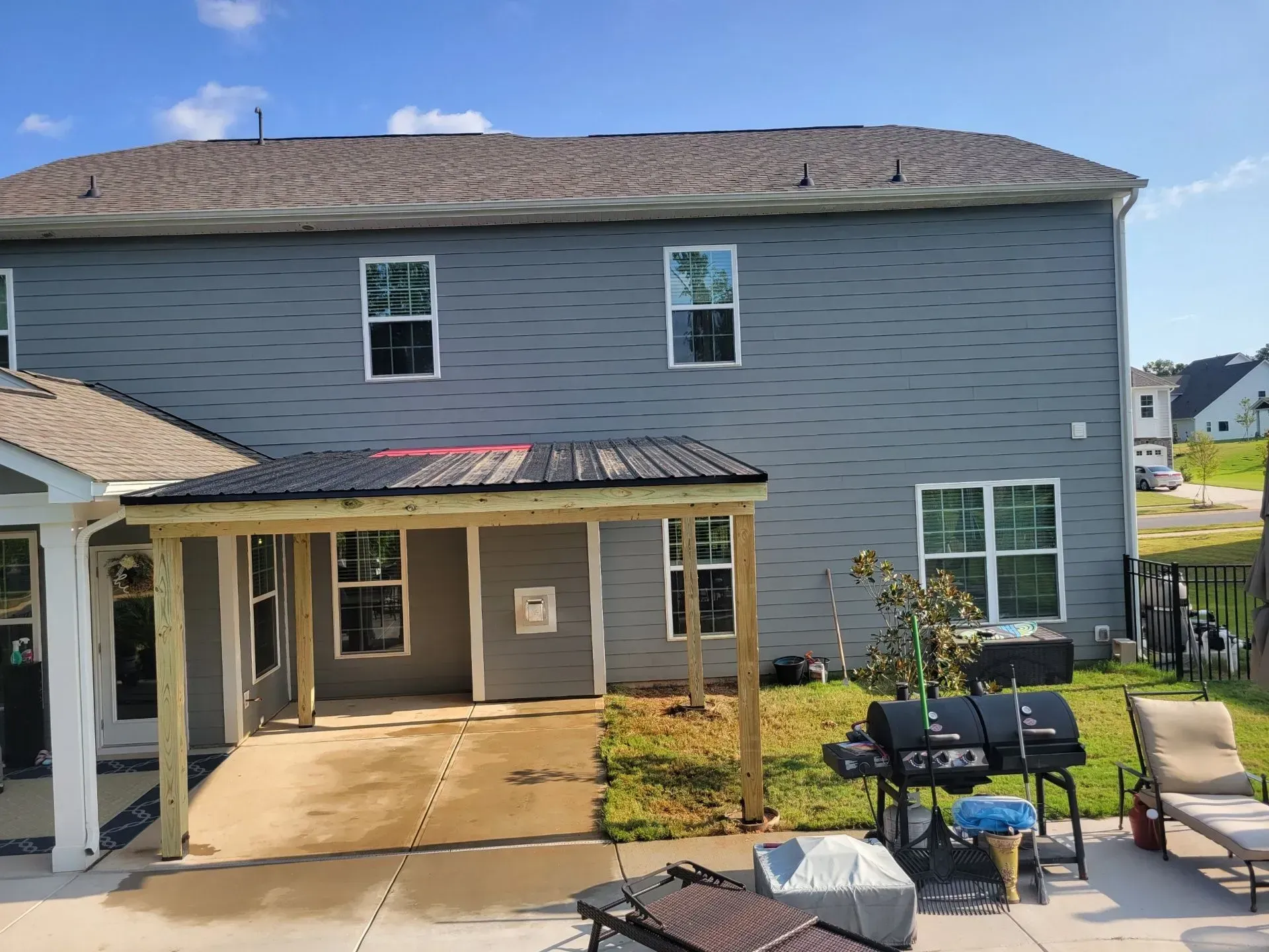 Two-story gray house with screened porch, patio furniture, and covered entryway under a blue sky