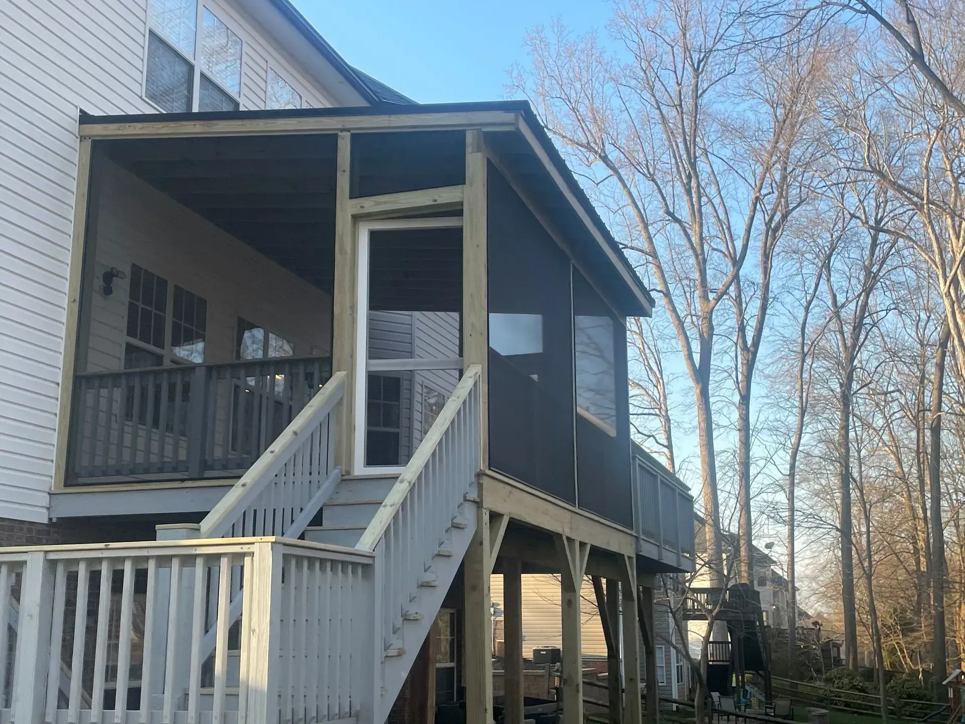 White wooden house porch with stairs and railing, elevated on stilts among leafless trees.