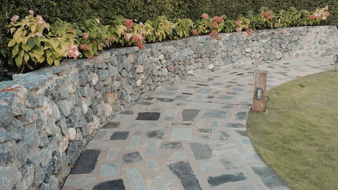 Curved stone garden path beside a low rock wall, with flowers and grass along the edge.