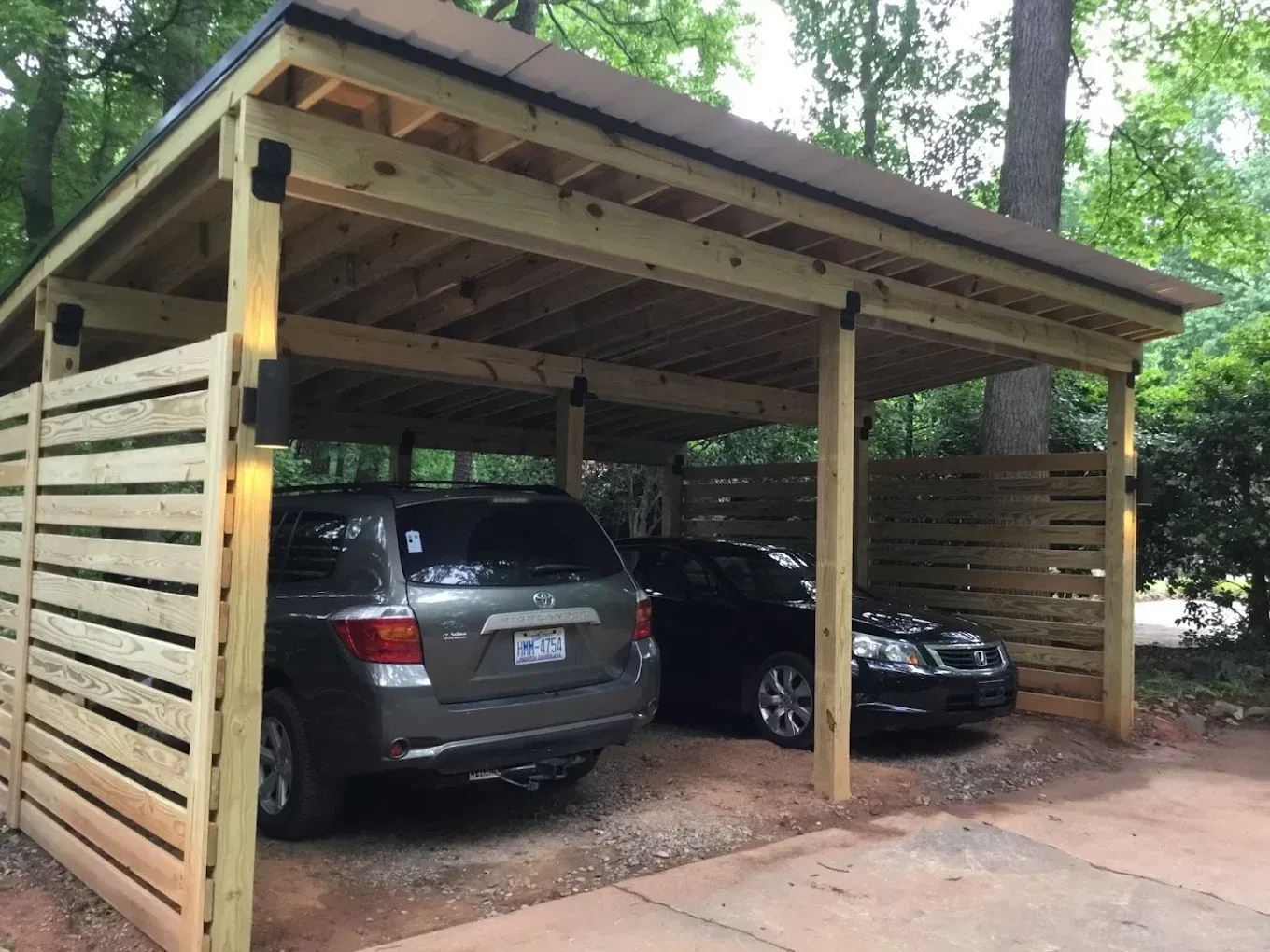 Wooden carport with a silver SUV and black sedan parked on gravel under a sloped roof