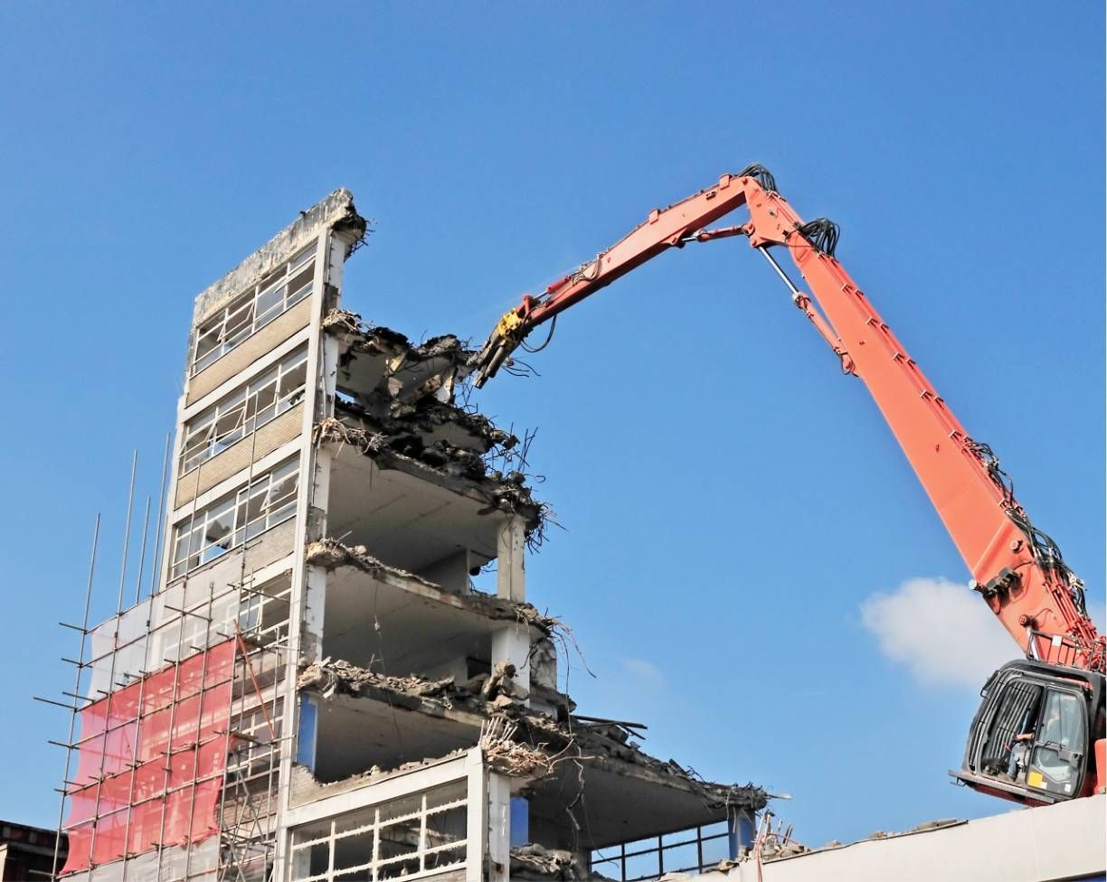 Excavator demolishing a partially collapsed building under a clear blue sky