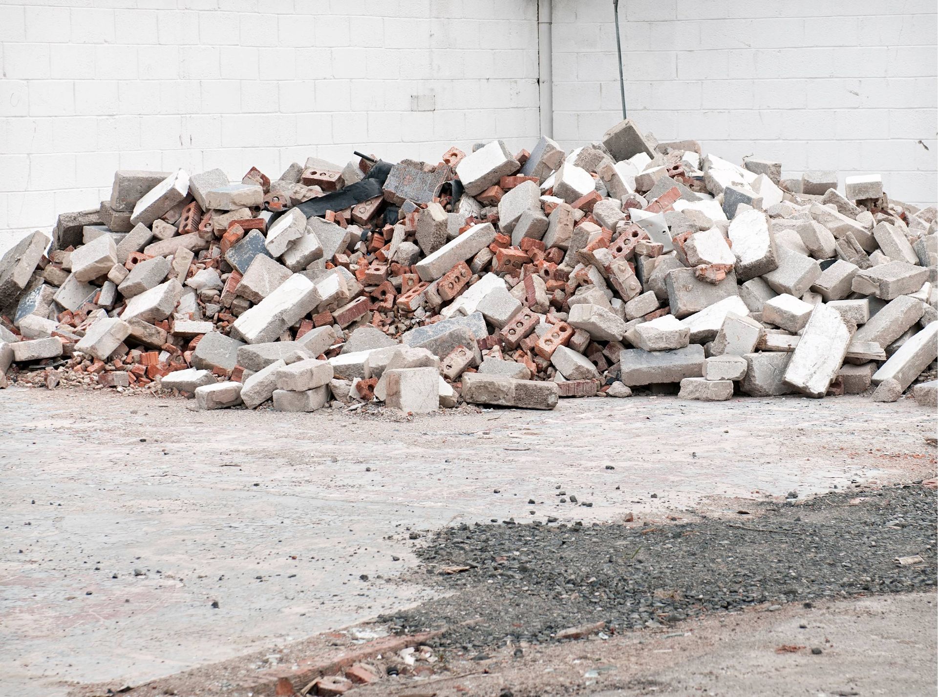 Pile of broken bricks and rubble on a concrete floor against a white wall.