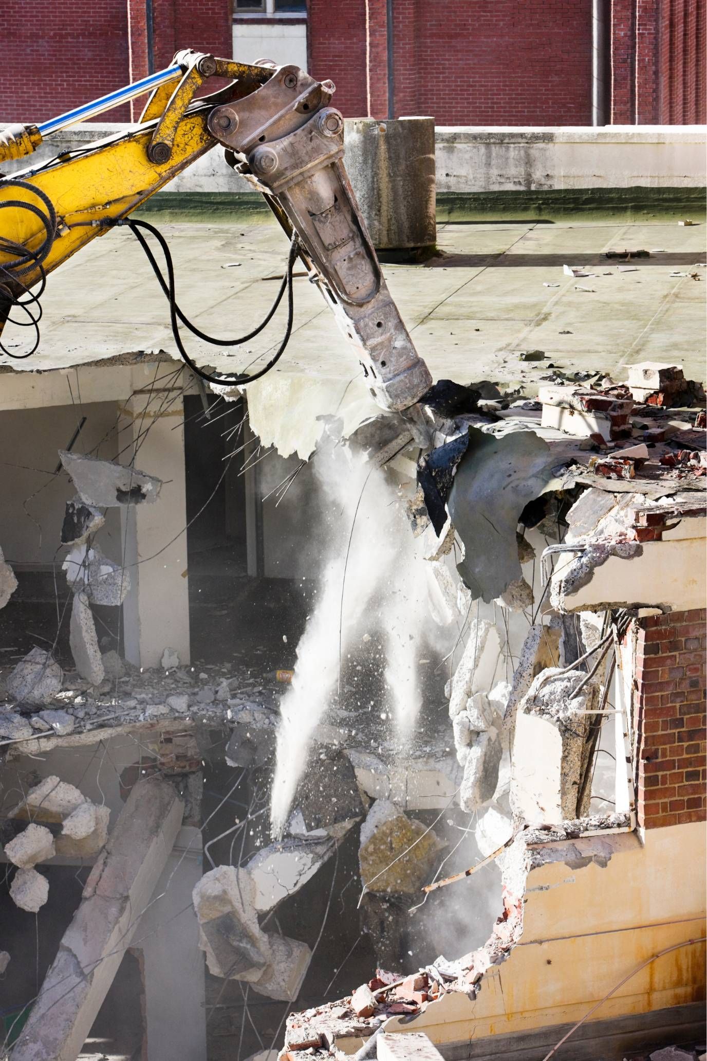 Excavator demolishing a damaged concrete wall amid debris and dust